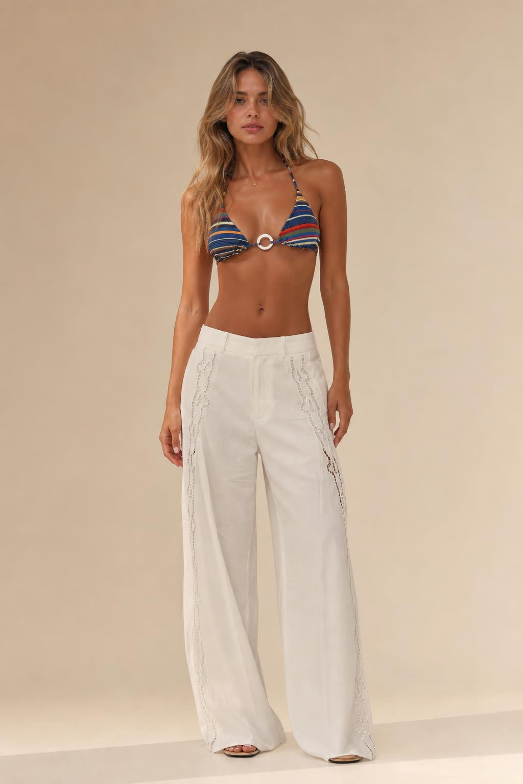 Woman standing in front view wearing white cutout wide leg trousers and patterned bikini top