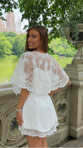 Back three-quarter view of white lace cape sleeve mini dress with scalloped hem