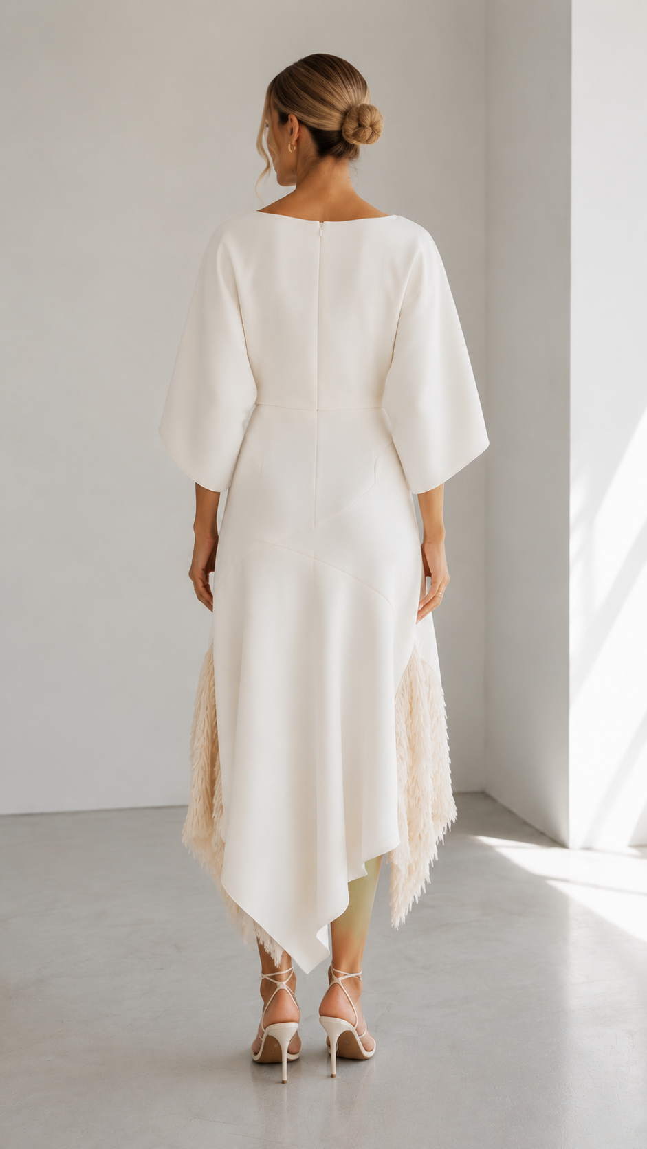 Back view of ivory asymmetric midi dress with cape sleeves and textured fringe hem