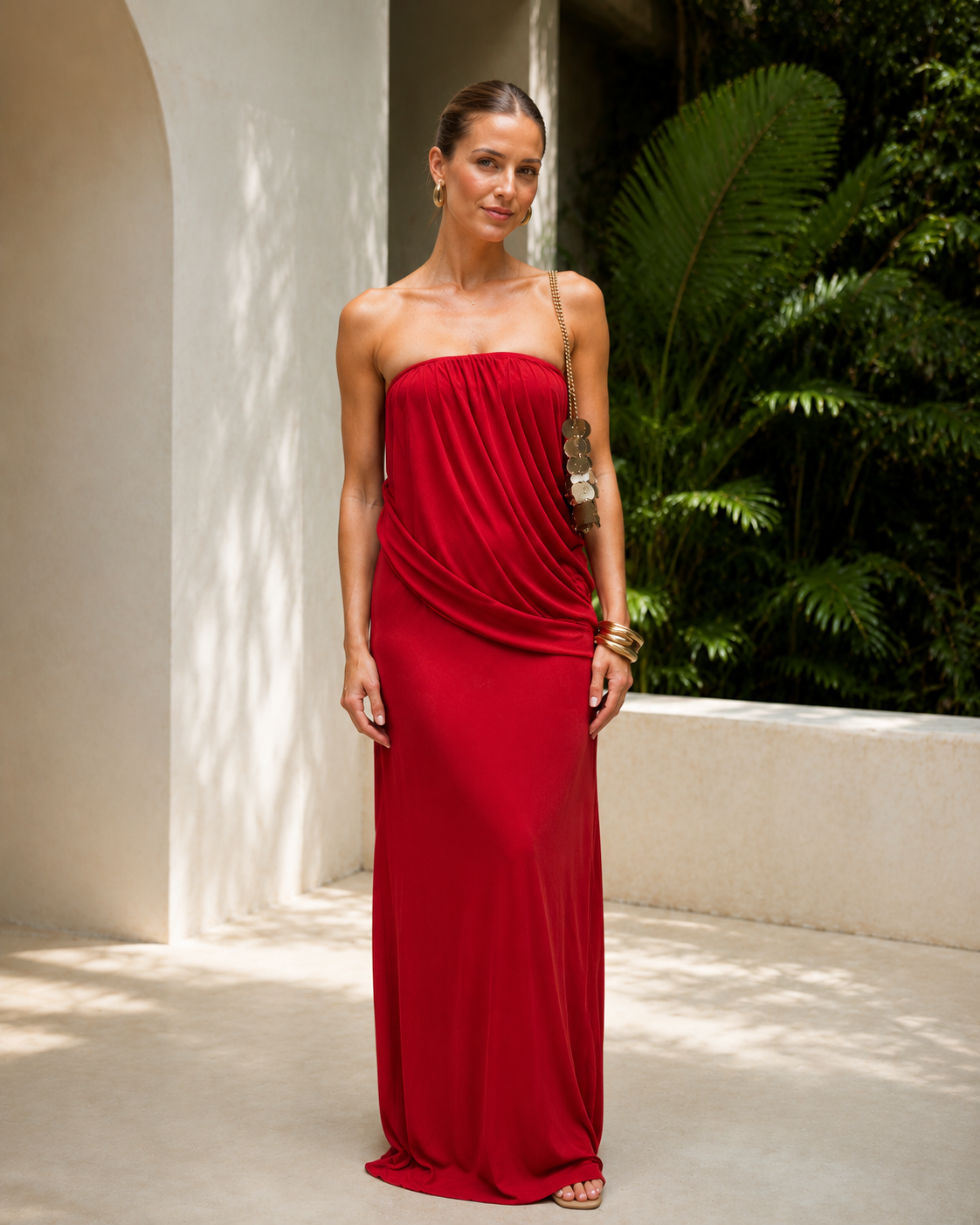 Front view of red strapless draped maxi dress styled with gold bangles