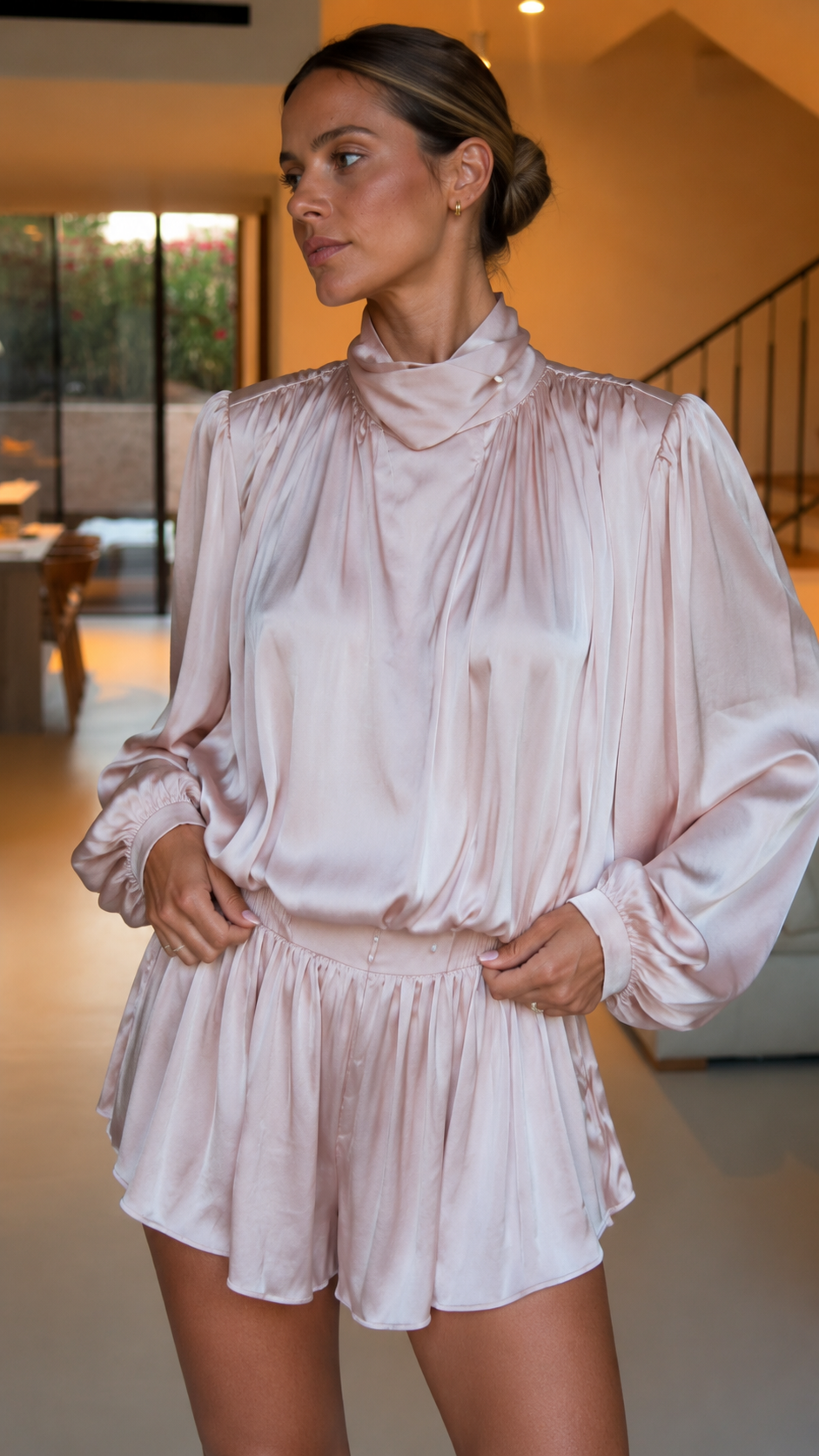Close-up of blush pink satin-look romper showing draped high neckline and gathered shoulders