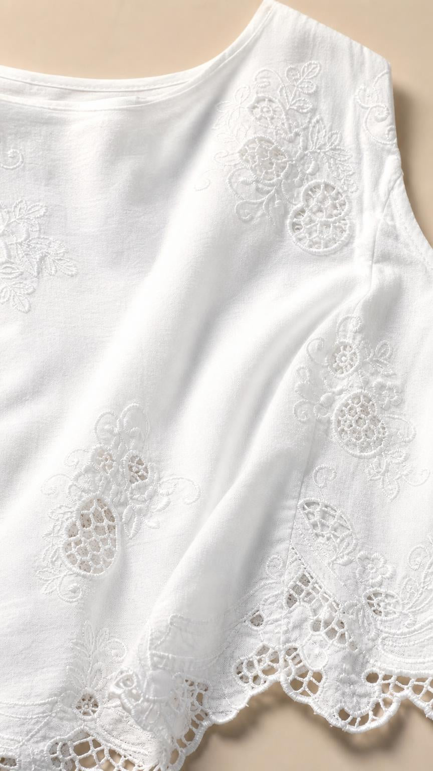 Close-up detail of white fabric with cut-out embroidery and scalloped hem