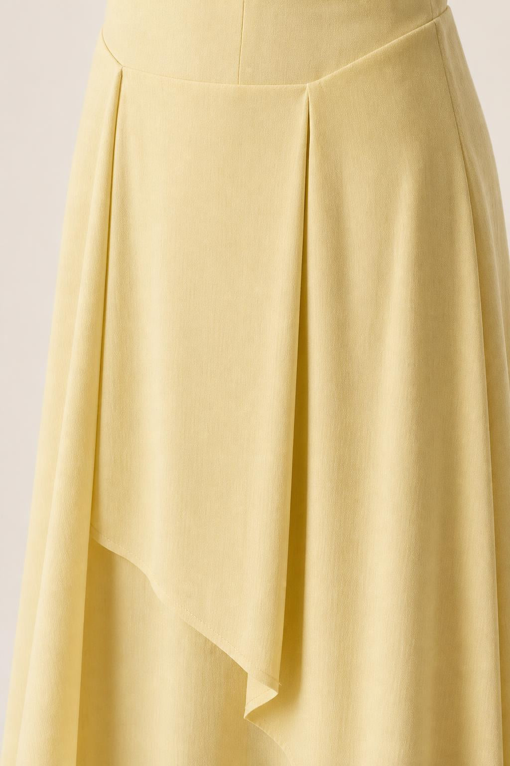 Close-up detail of pleated waist and asymmetric layered skirt on yellow dress