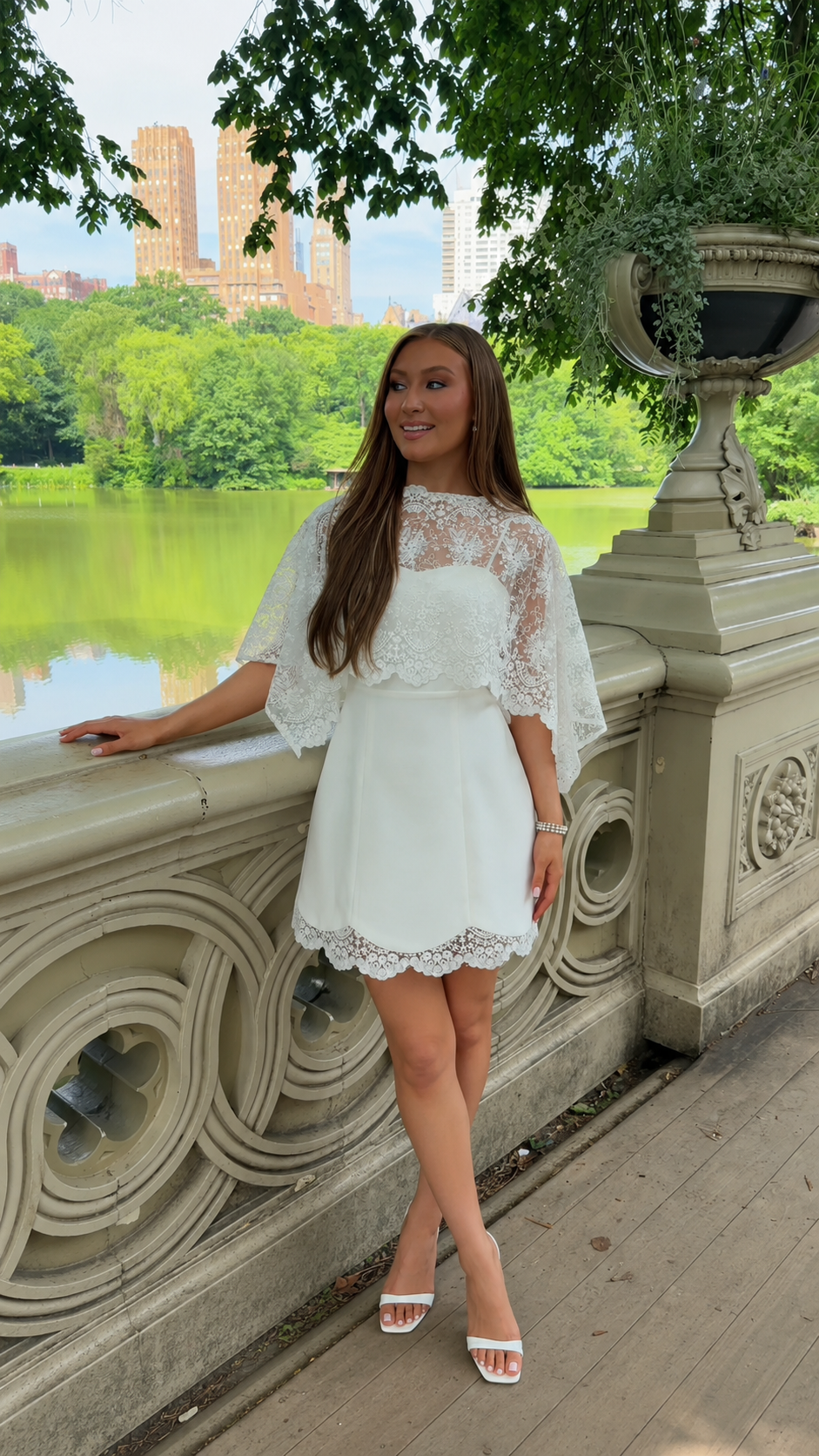 Front angled view of white lace cape sleeve mini dress with strappy heels