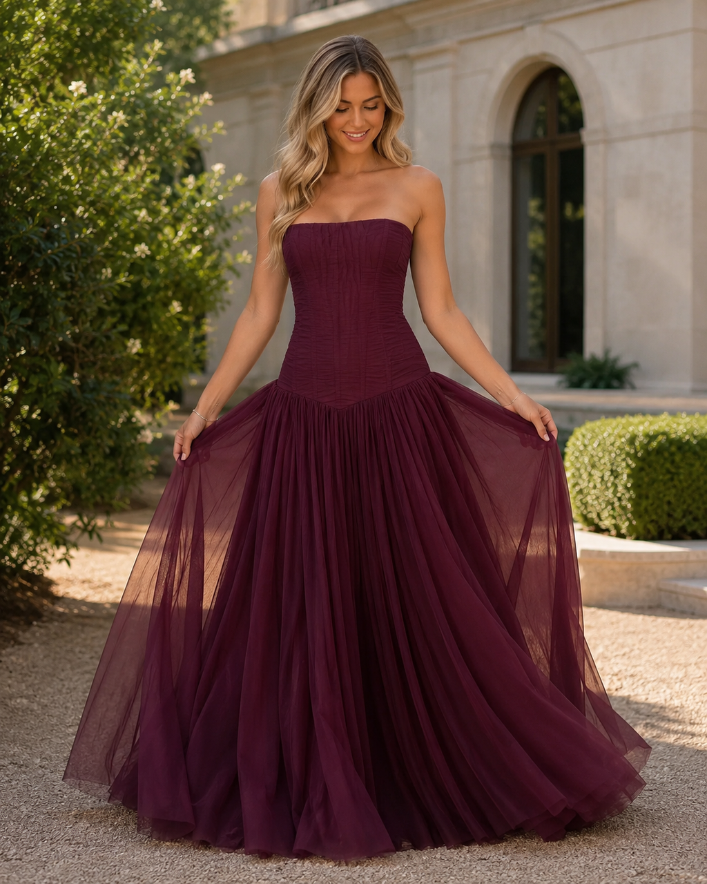 Front angled view of burgundy strapless corset-style gown with sheer overlay skirt